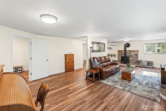 living room with a wood stove, an AC wall unit, a textured ceiling, wood finished floors, and baseboards