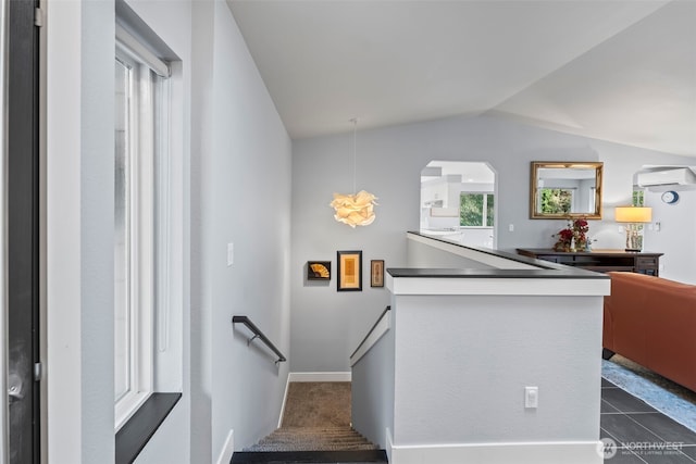 staircase featuring lofted ceiling, baseboards, a wall unit AC, and arched walkways