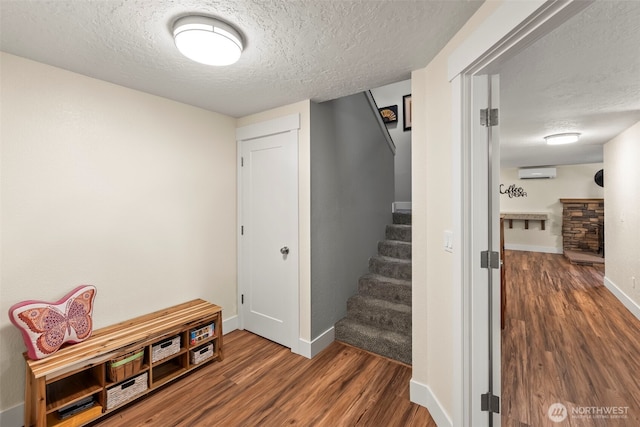 stairs with baseboards, a wall unit AC, wood finished floors, a textured ceiling, and a fireplace