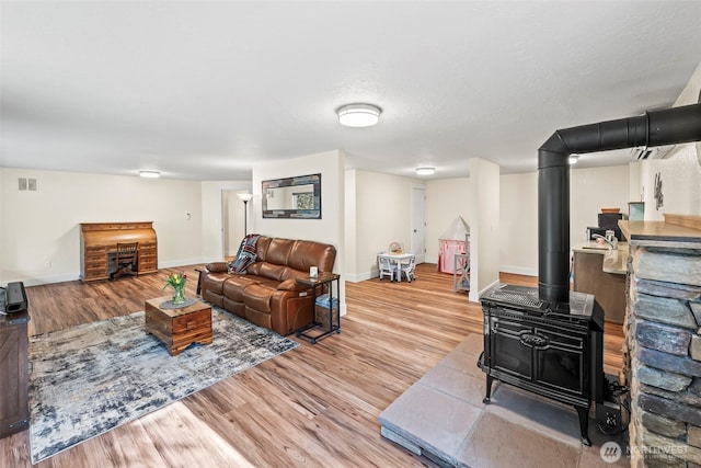 living room featuring a wood stove, visible vents, baseboards, and wood finished floors