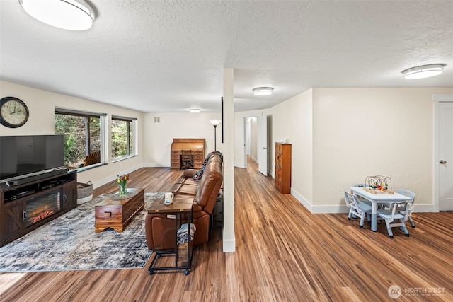 living area with a textured ceiling, wood finished floors, a glass covered fireplace, and baseboards