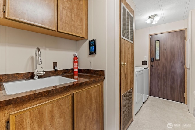 laundry area with washing machine and clothes dryer, cabinet space, visible vents, a sink, and a textured ceiling