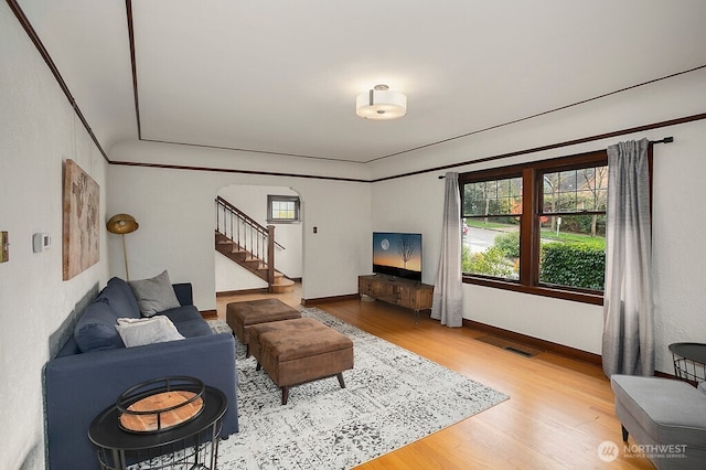 living area featuring wood finished floors, visible vents, baseboards, ornamental molding, and stairway