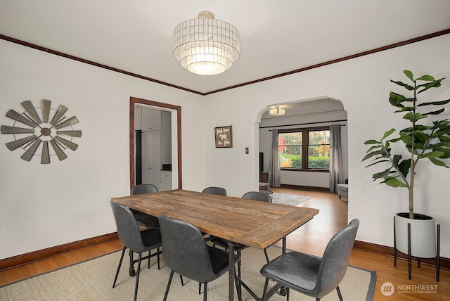 dining space featuring light wood-style flooring, arched walkways, baseboards, and ornamental molding