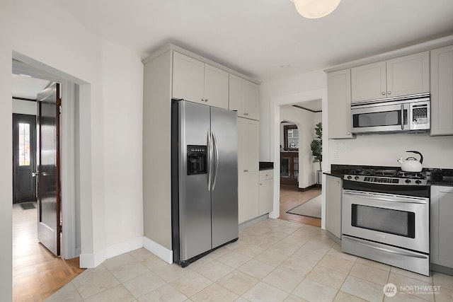 kitchen with light tile patterned floors, gray cabinetry, stainless steel appliances, baseboards, and dark countertops