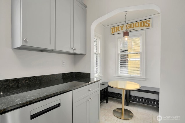 kitchen featuring dark stone counters, hanging light fixtures, arched walkways, and light tile patterned floors