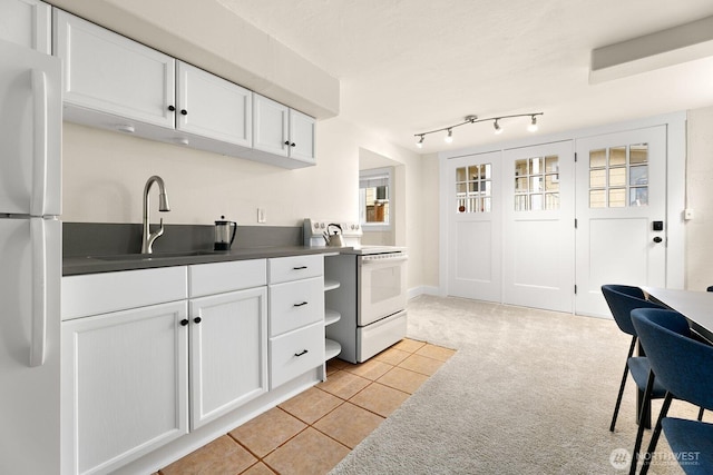 kitchen featuring dark countertops, light carpet, a sink, white cabinets, and white appliances