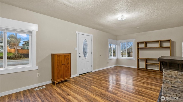 foyer with a textured ceiling, wood finished floors, visible vents, and baseboards