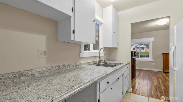 kitchen featuring light tile patterned floors, a sink, white cabinetry, baseboards, and freestanding refrigerator