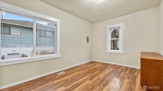 unfurnished room with a textured ceiling, wood finished floors, visible vents, and baseboards