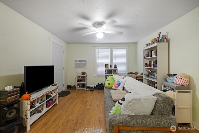 bedroom featuring an AC wall unit, light wood-type flooring, a ceiling fan, and baseboards