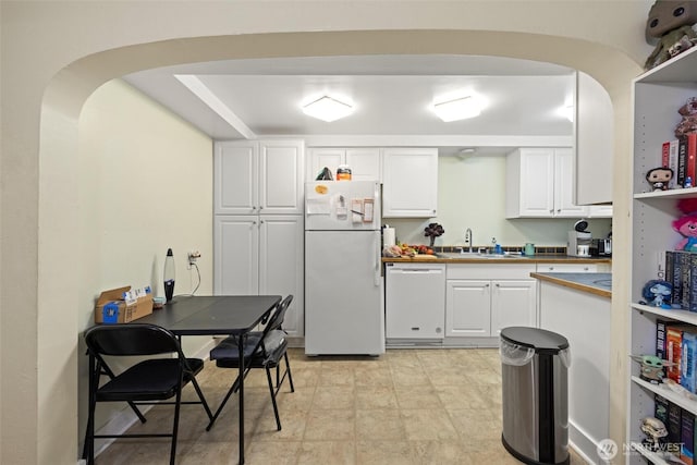 kitchen with arched walkways, white appliances, a sink, and white cabinetry