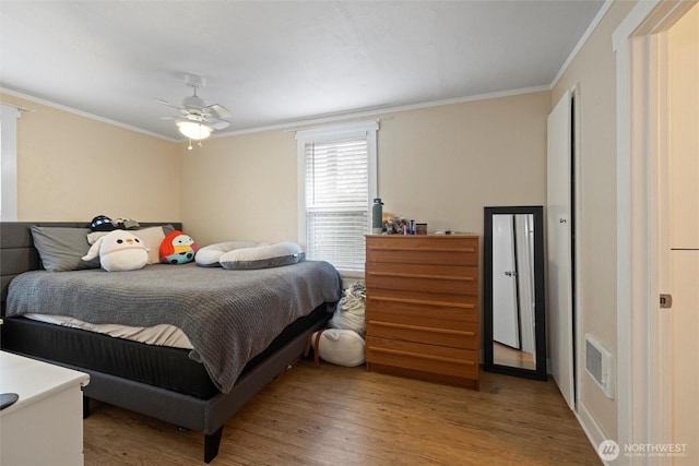 bedroom with light wood finished floors, visible vents, ornamental molding, and a ceiling fan