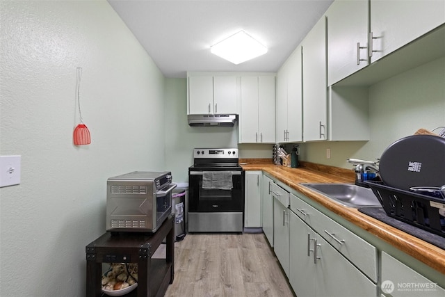 kitchen with under cabinet range hood, a sink, white cabinetry, light wood-style floors, and stainless steel electric range