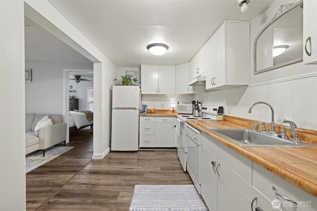 kitchen with white appliances, dark wood-style flooring, under cabinet range hood, white cabinetry, and a sink