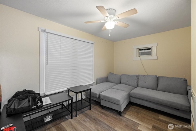 living area with an AC wall unit, ceiling fan, and wood finished floors