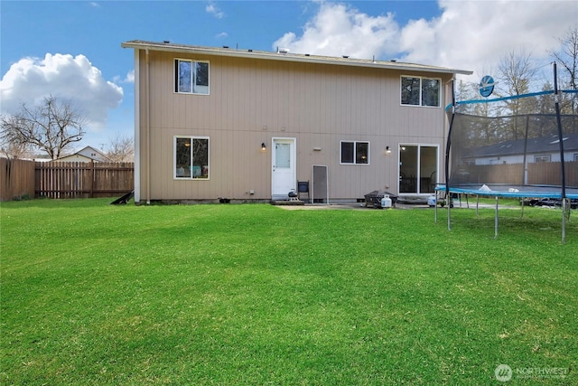 back of house featuring a trampoline, fence, and a lawn