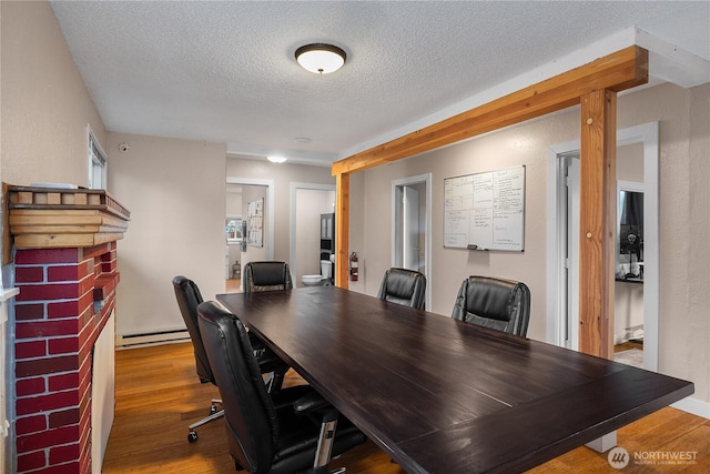 office space featuring a textured ceiling, a fireplace, a baseboard radiator, and wood finished floors