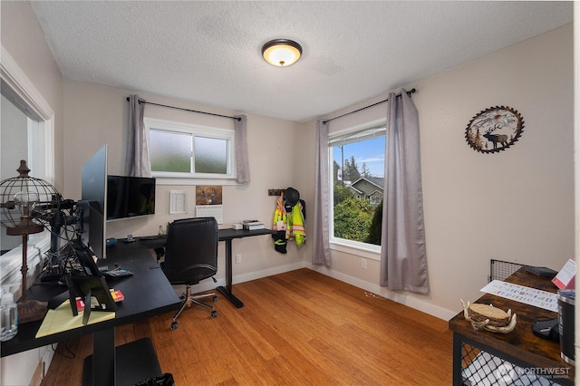 home office with light wood-style flooring, baseboards, and a textured ceiling