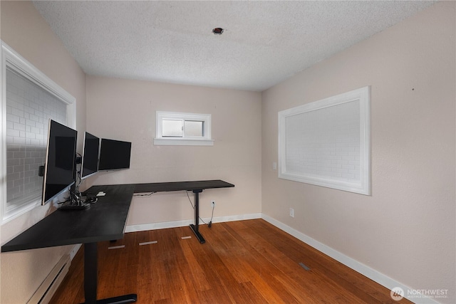 office space with a baseboard heating unit, a textured ceiling, baseboards, and wood finished floors