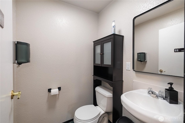 half bathroom featuring a textured wall, a sink, and toilet