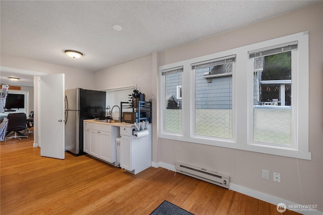 kitchen featuring light wood-type flooring, white cabinetry, baseboard heating, and a textured ceiling