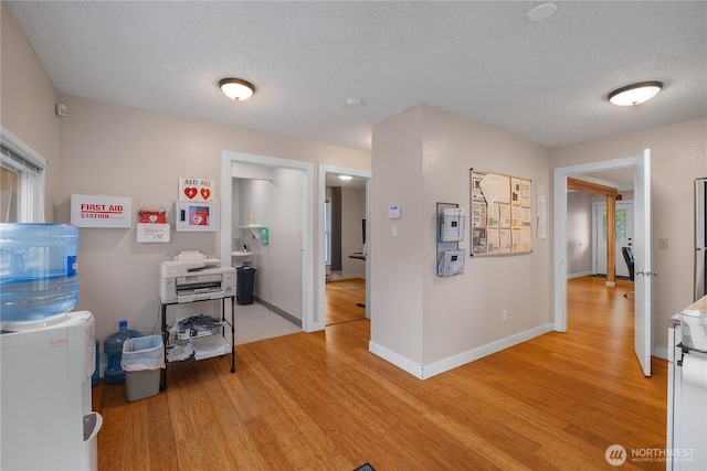 interior space with a textured ceiling, light wood finished floors, and baseboards