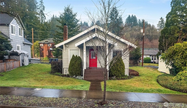 bungalow-style home with a front yard, fence, and a chimney