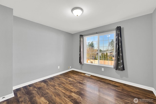 spare room with dark wood-style floors, visible vents, and baseboards