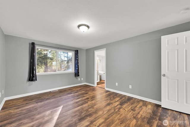 unfurnished bedroom with visible vents, baseboards, dark wood finished floors, and ensuite bathroom