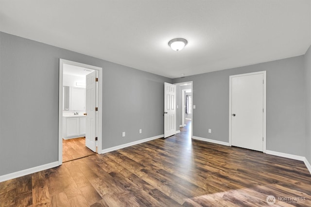 unfurnished bedroom featuring ensuite bath, dark wood finished floors, and baseboards