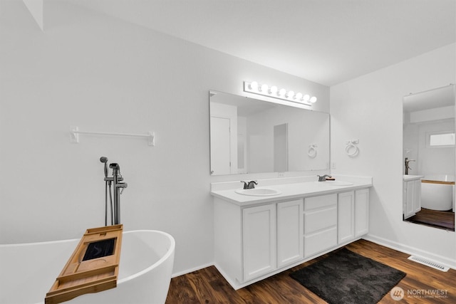 full bathroom featuring a freestanding bath, double vanity, a sink, and visible vents