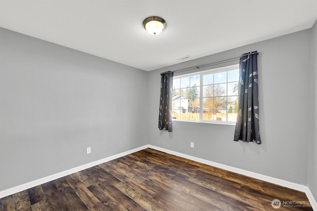 spare room featuring dark wood-style floors, visible vents, and baseboards