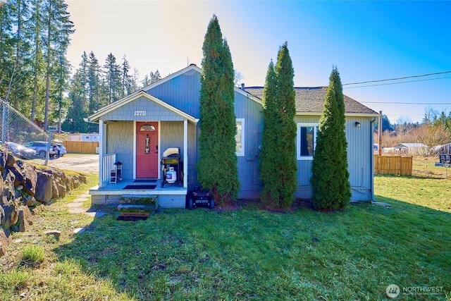 view of front of property featuring covered porch, roof with shingles, a front yard, and fence