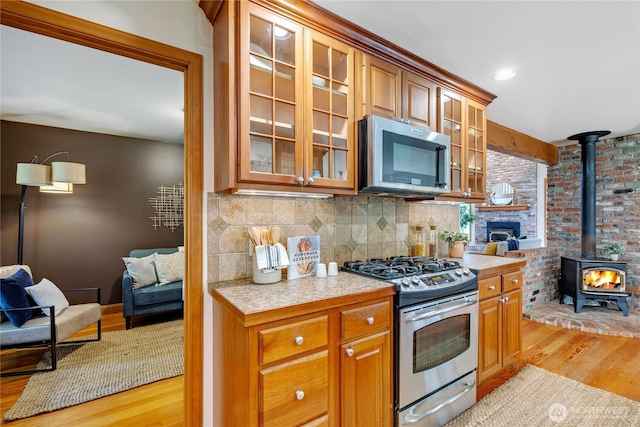 kitchen featuring light wood finished floors, glass insert cabinets, a wood stove, stainless steel appliances, and light countertops