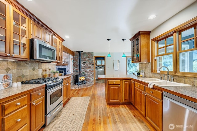 kitchen featuring a peninsula, a sink, appliances with stainless steel finishes, brown cabinetry, and a wood stove