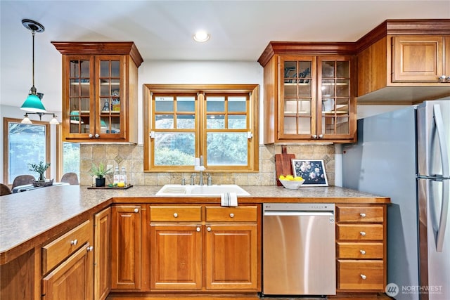 kitchen featuring stainless steel appliances, brown cabinetry, a sink, and a wealth of natural light