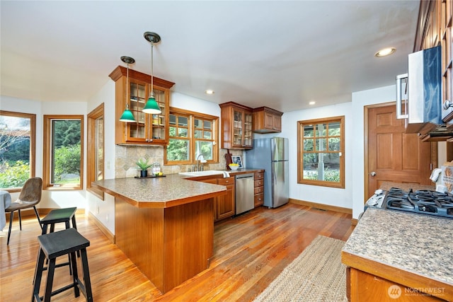 kitchen with brown cabinetry, decorative backsplash, a peninsula, stainless steel appliances, and a sink