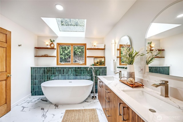 bathroom featuring a freestanding bath, marble finish floor, a skylight, and a sink