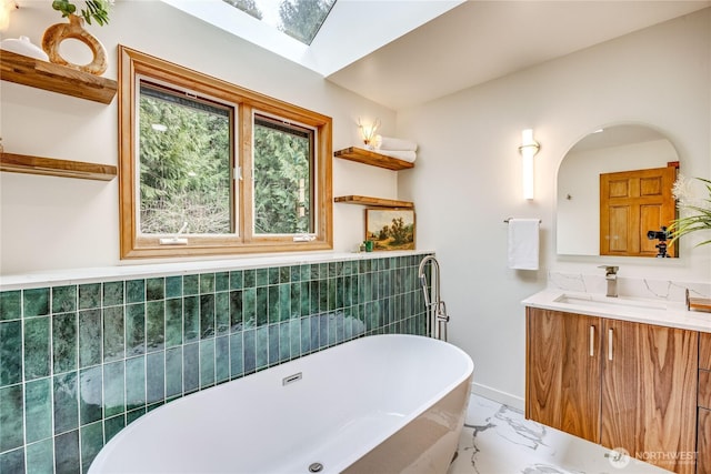 bathroom with marble finish floor, a skylight, a freestanding tub, and vanity