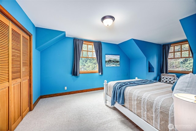 carpeted bedroom with lofted ceiling, a closet, and baseboards