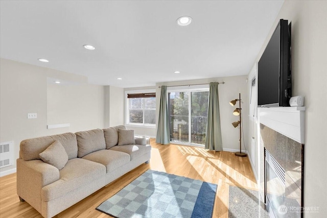 living room featuring light wood finished floors, a fireplace with flush hearth, baseboards, and recessed lighting