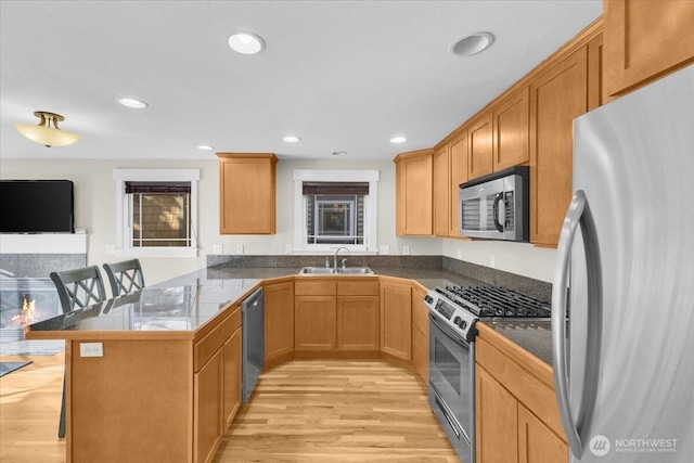 kitchen with a breakfast bar area, a peninsula, a sink, appliances with stainless steel finishes, and light wood finished floors