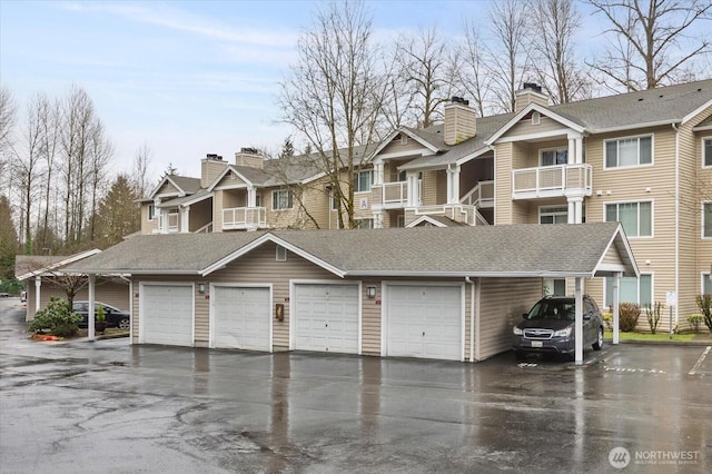 view of front facade with roof with shingles, a residential view, a chimney, and community garages