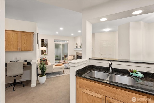 kitchen featuring light carpet, dark stone counters, a fireplace, a sink, and recessed lighting