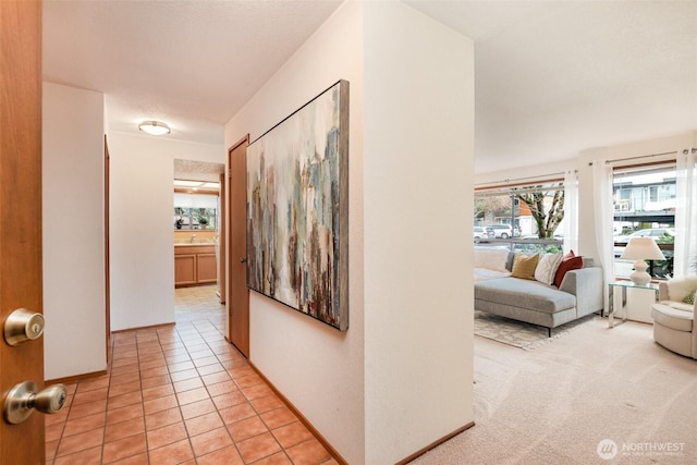 hall featuring light tile patterned floors, light carpet, a sink, and baseboards