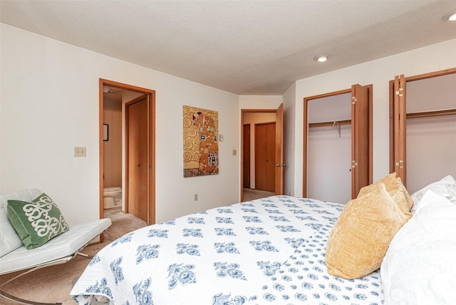 bedroom featuring light carpet, a textured ceiling, and two closets