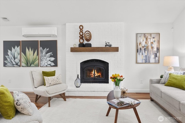 living area featuring a fireplace, a wall mounted air conditioner, wood finished floors, and baseboards