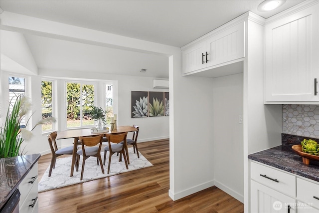 interior space with lofted ceiling, a wall unit AC, wood finished floors, and baseboards