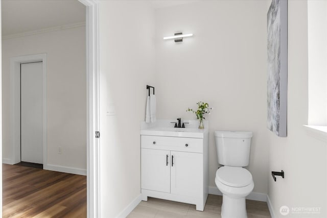 bathroom with toilet, wood finished floors, vanity, baseboards, and crown molding